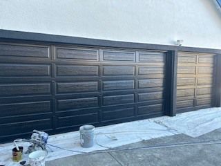 Black painted garage doors with dark trim and painting supplies on the ground.