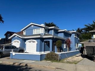 Blue two-story house with white trim and garage doors on a sunny day.