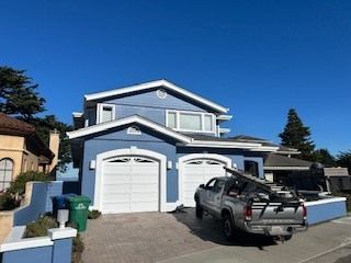 Blue house with white garage doors, a truck parked in the driveway, and a blue sky overhead.