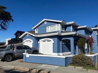 Blue house with white trim, two-car garage, and gray truck parked outside on a sunny day.