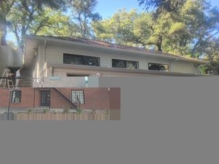 Beige and brick building with multiple windows, set against a backdrop of green trees.