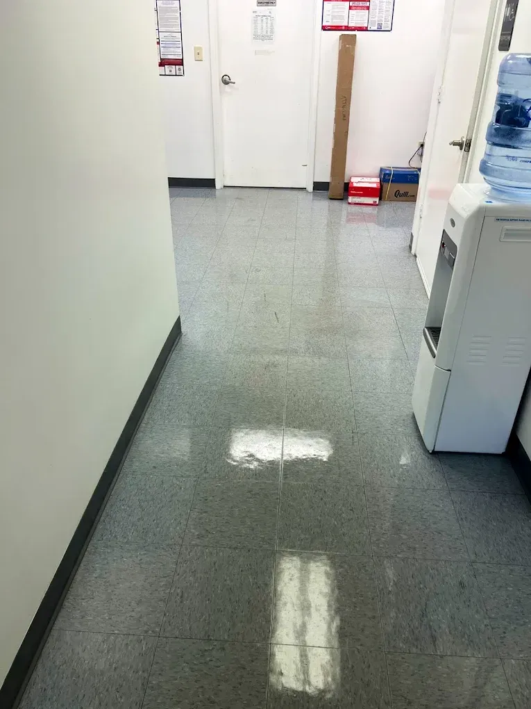 A narrow office hallway with speckled gray flooring, a water cooler, and closed doors.
