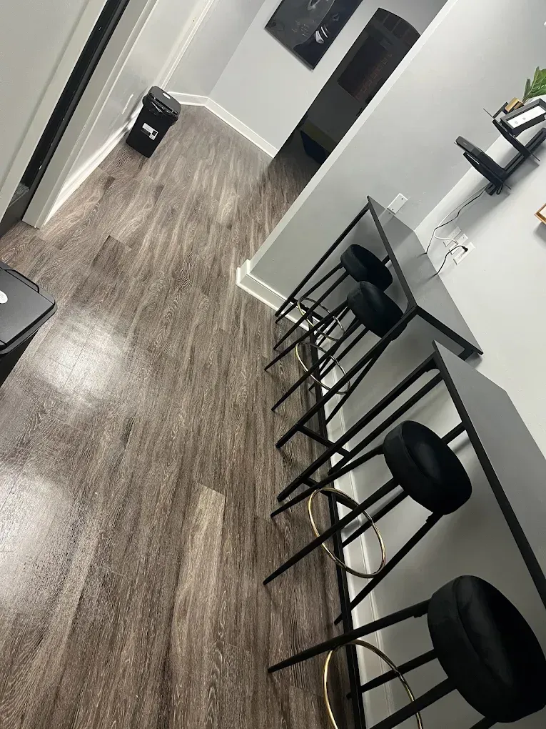 Dark wood-look flooring with a row of black bar stools along a counter, white walls.