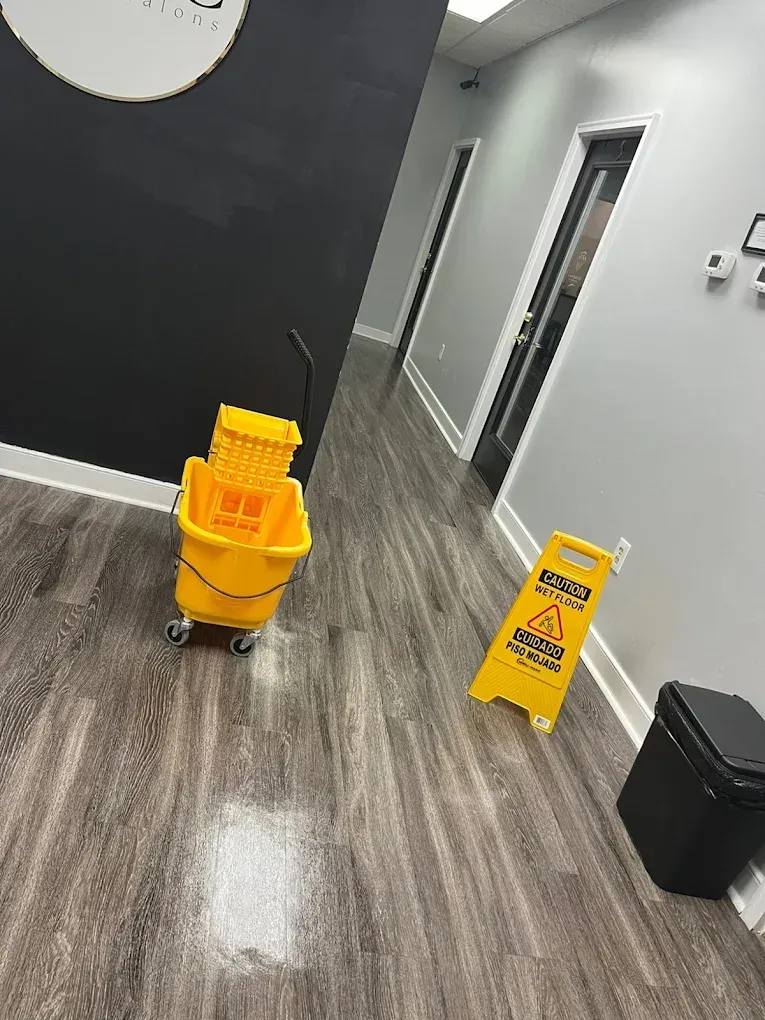 Yellow mop bucket and wet floor sign in a gray-walled hallway with dark wood-look flooring.