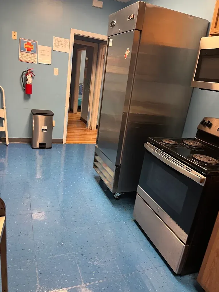 Kitchen with blue floor, stainless steel fridge, stove, and a doorway leading to a hallway.