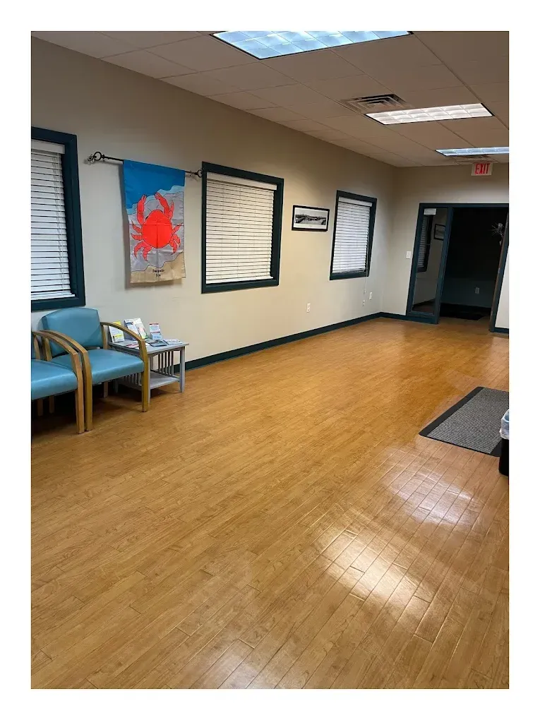 Waiting room with blue chairs, artwork, and wood flooring.