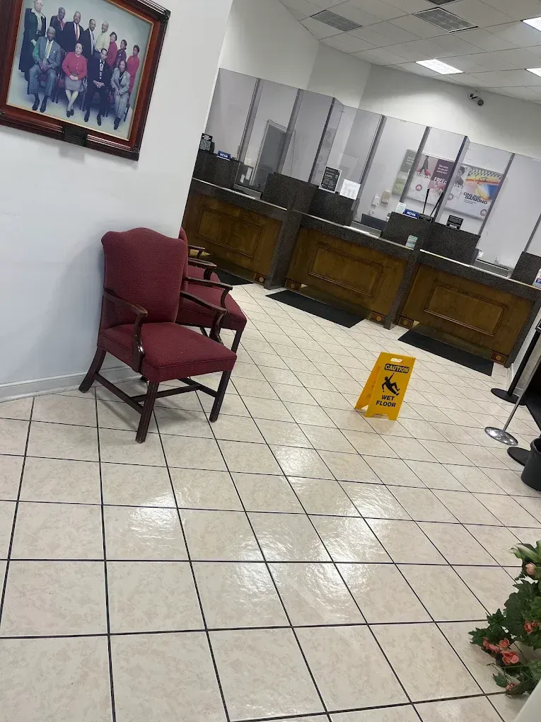 An interior view of a bank lobby with seating, counters, and a wet floor sign.
