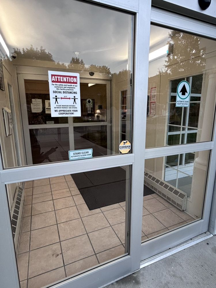 Glass entrance doors with social distancing signs. Inside, tiled floor and a doorway.