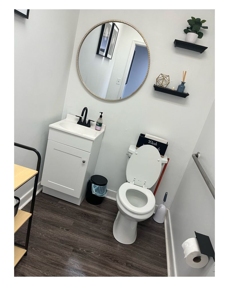 Small bathroom with toilet, sink, mirror, and black shelves with decorative items.