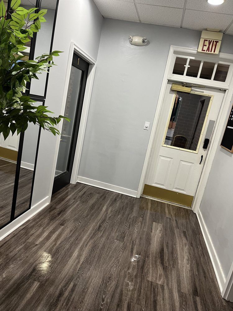 Hallway with gray walls, dark wood floor, and two doors: one black and one white with exit sign.
