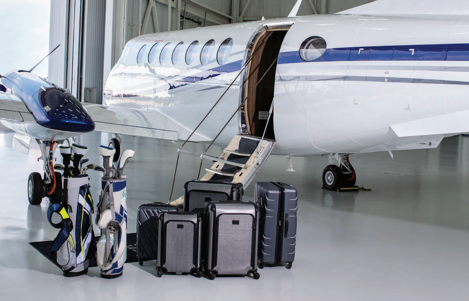 A private jet is parked in a hangar with luggage and golf clubs.