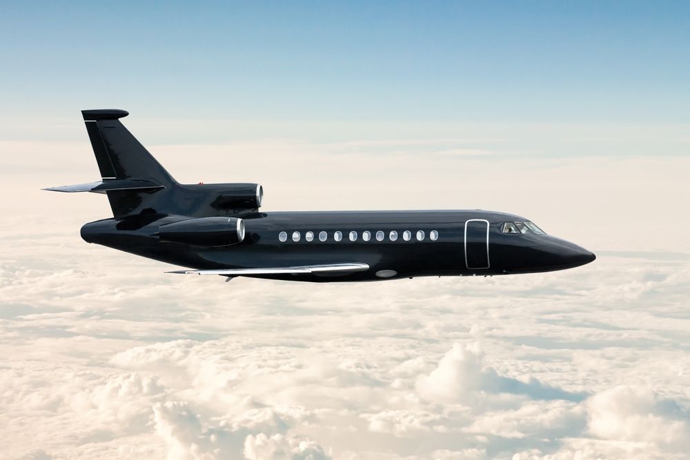 A black private jet is flying in the sky above the clouds.