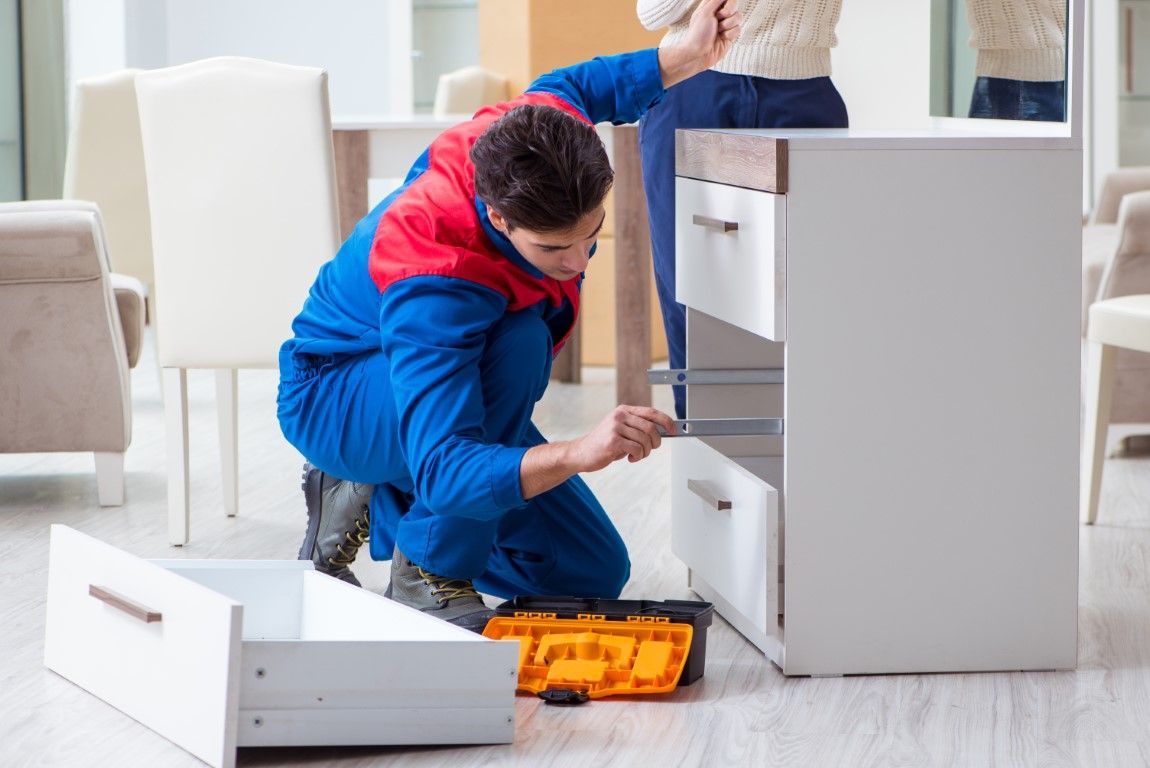 Person assembling white furniture in a bright room, with tools spread on the floor.