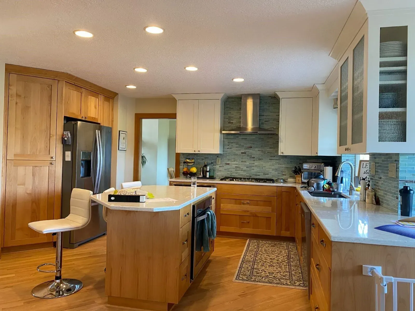 A spacious kitchen with natural wood cabinets, white countertops, a center island, and blue-gray tiled backsplash.