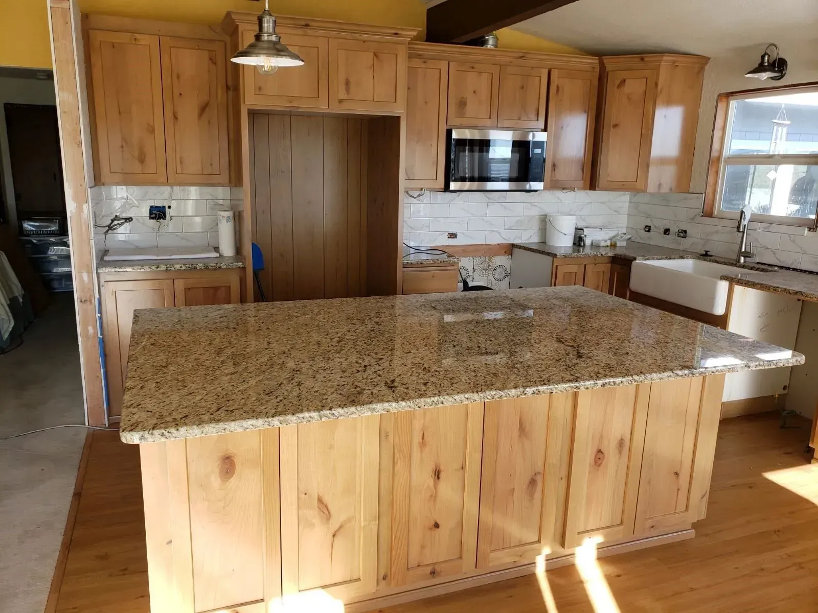 A rustic kitchen featuring knotty pine cabinets, a large granite-topped island, and white tile backsplashes.