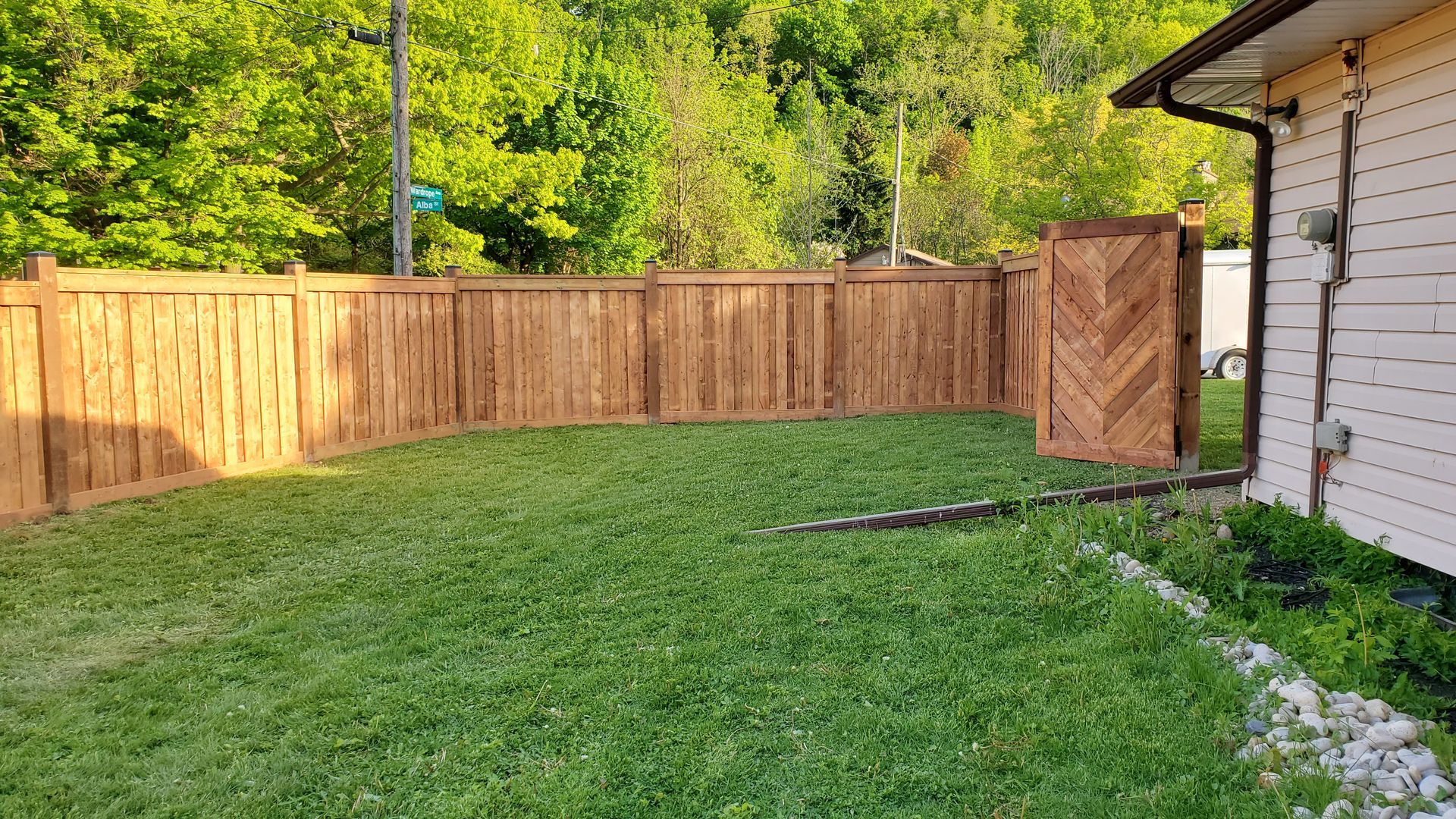Grassy backyard with wooden fence, open gate, and white house wall on the right.