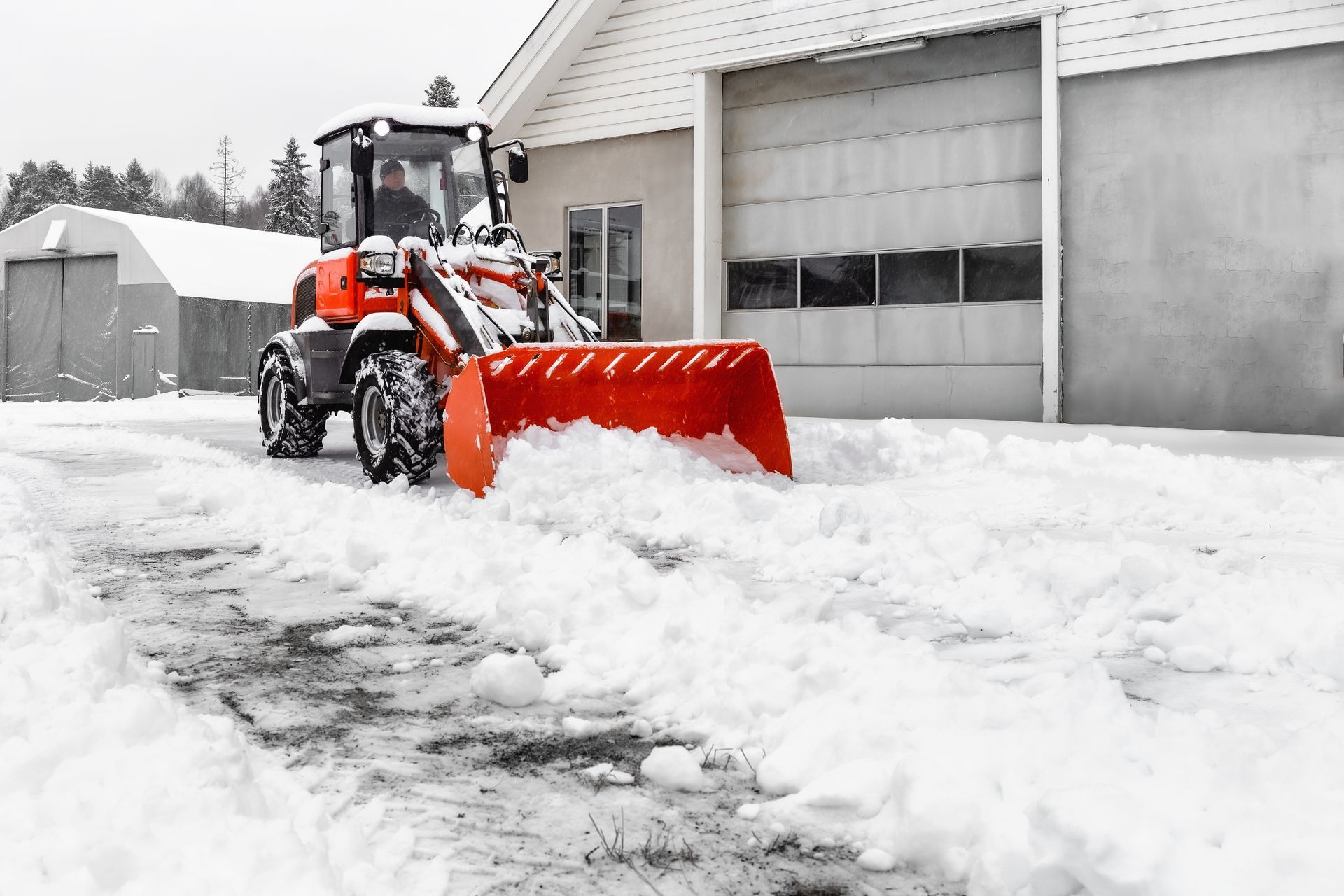 A red front loader plowing snow from a driveway in front of a building on a snowy day.