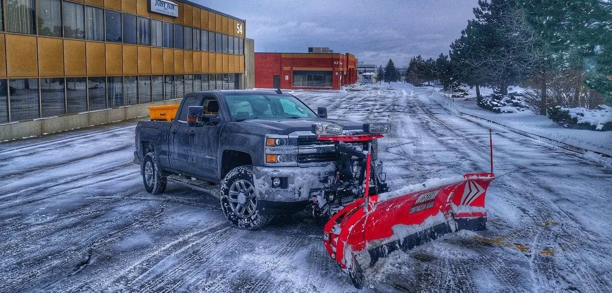 A snow plow truck clearing a snow-covered street in front of a building.