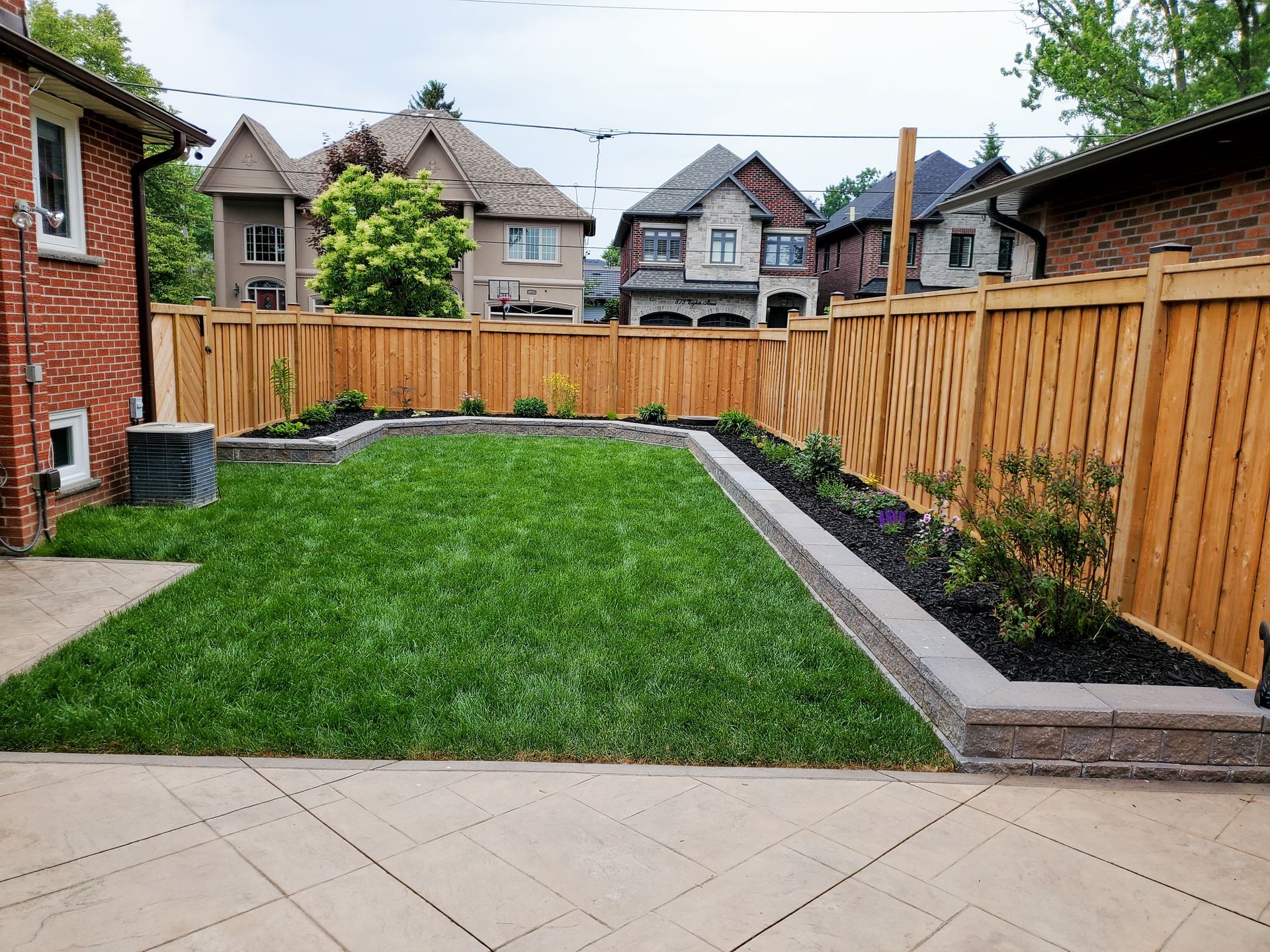 a backyard with a wooden fence and a brick house in the background .