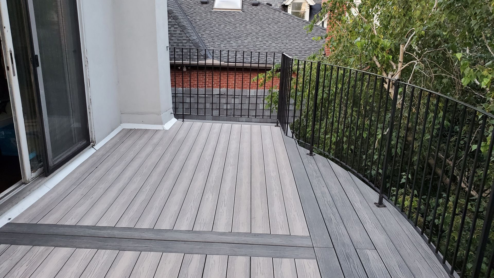 Empty gray balcony deck with black railings and a small gate, overlooking trees and a street below