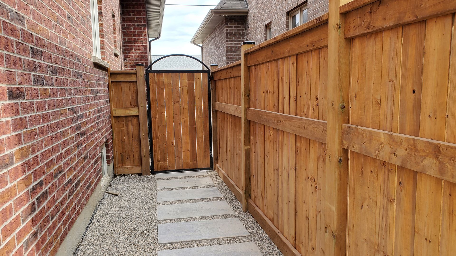 Wooden fence with a gate leading to the side of a brick building. Gray stepping stones.