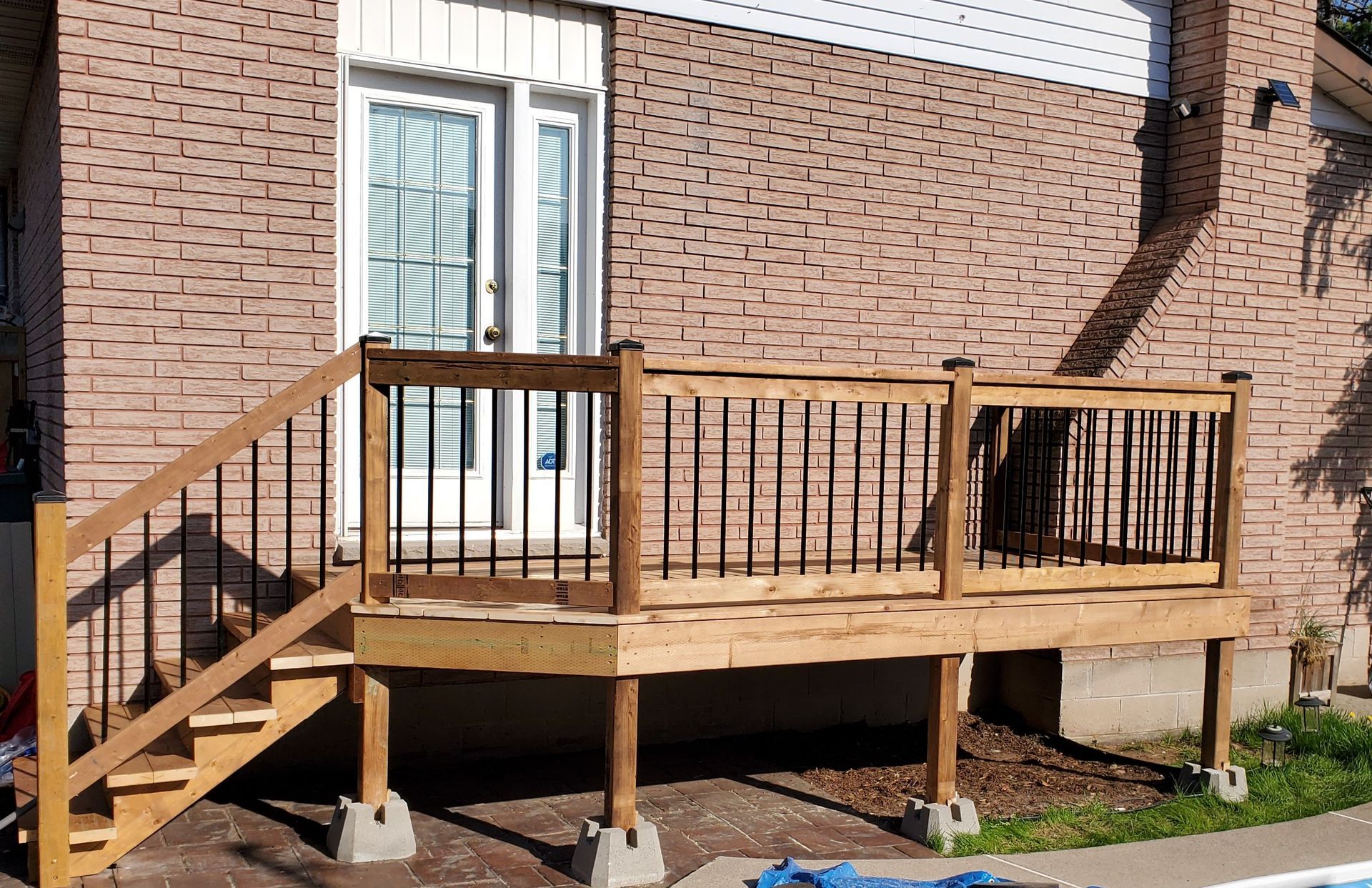 a wooden deck with stairs is in front of a brick house next to a pool .