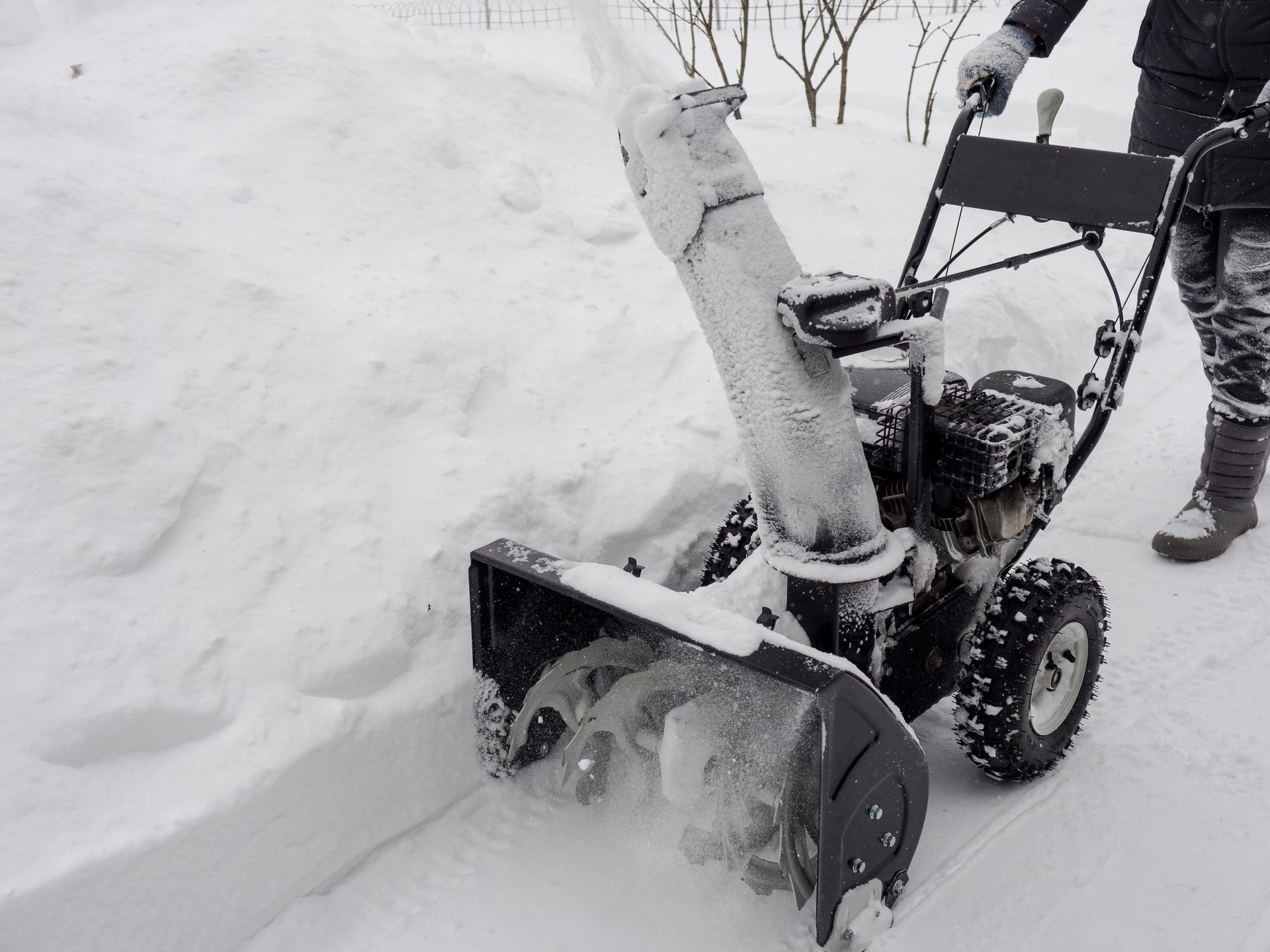 a person is using a snow blower to clear snow from a sidewalk .