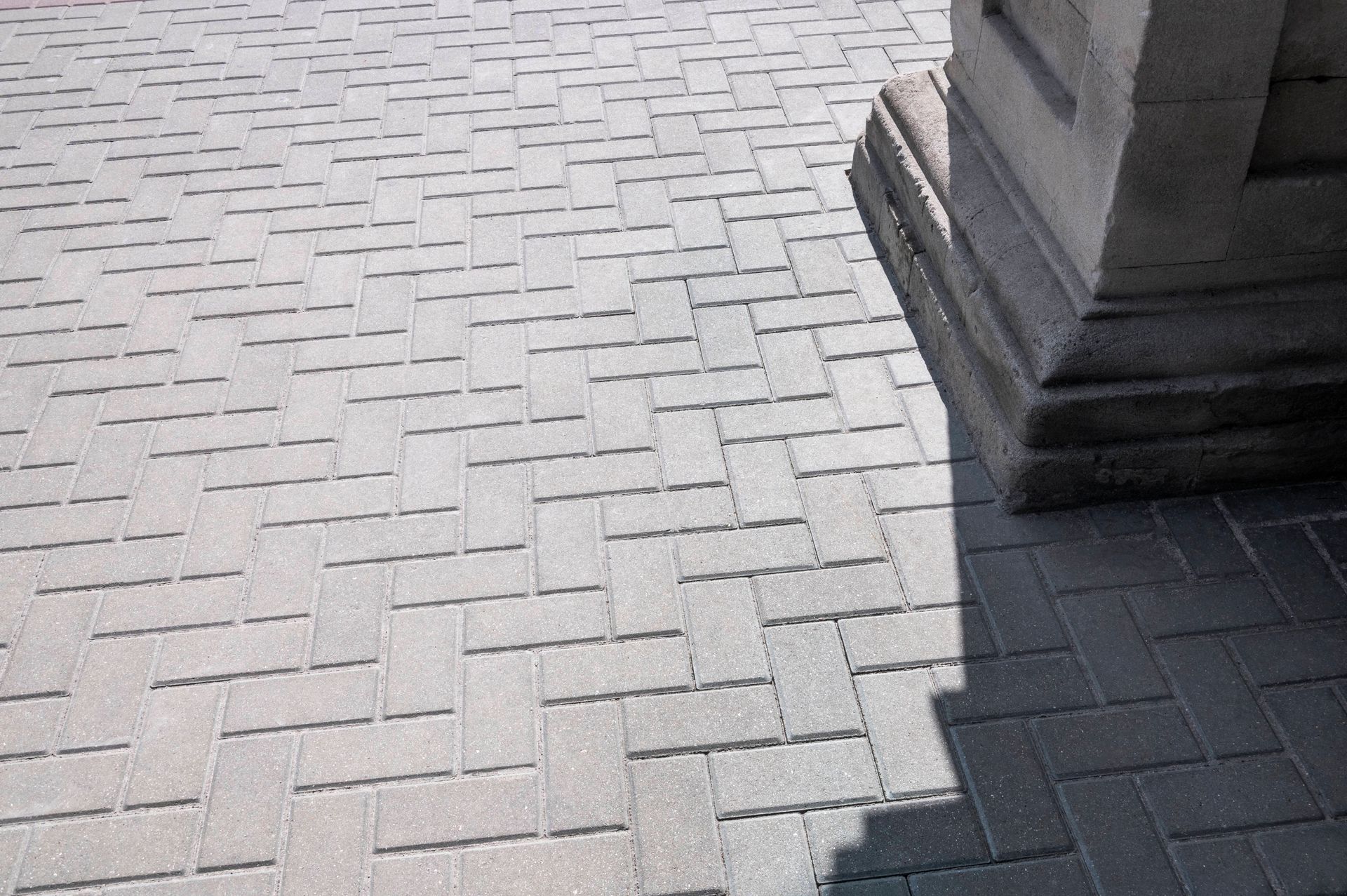 a shadow of a column is cast on a brick pavement