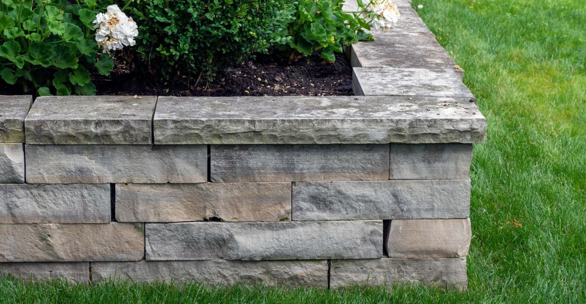 a stone wall surrounds a flower bed with white flowers