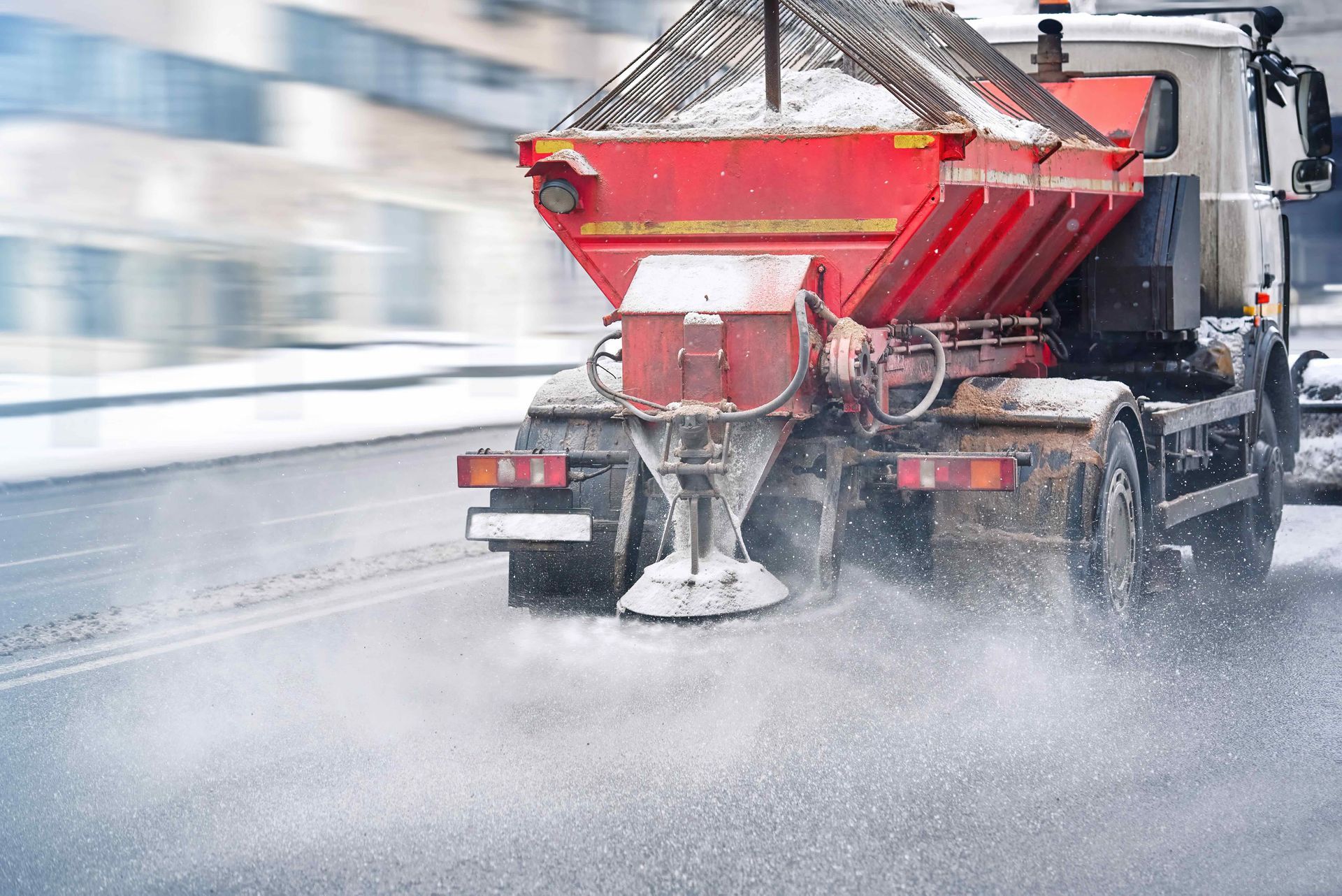 a red and white truck is spreading salt on the road