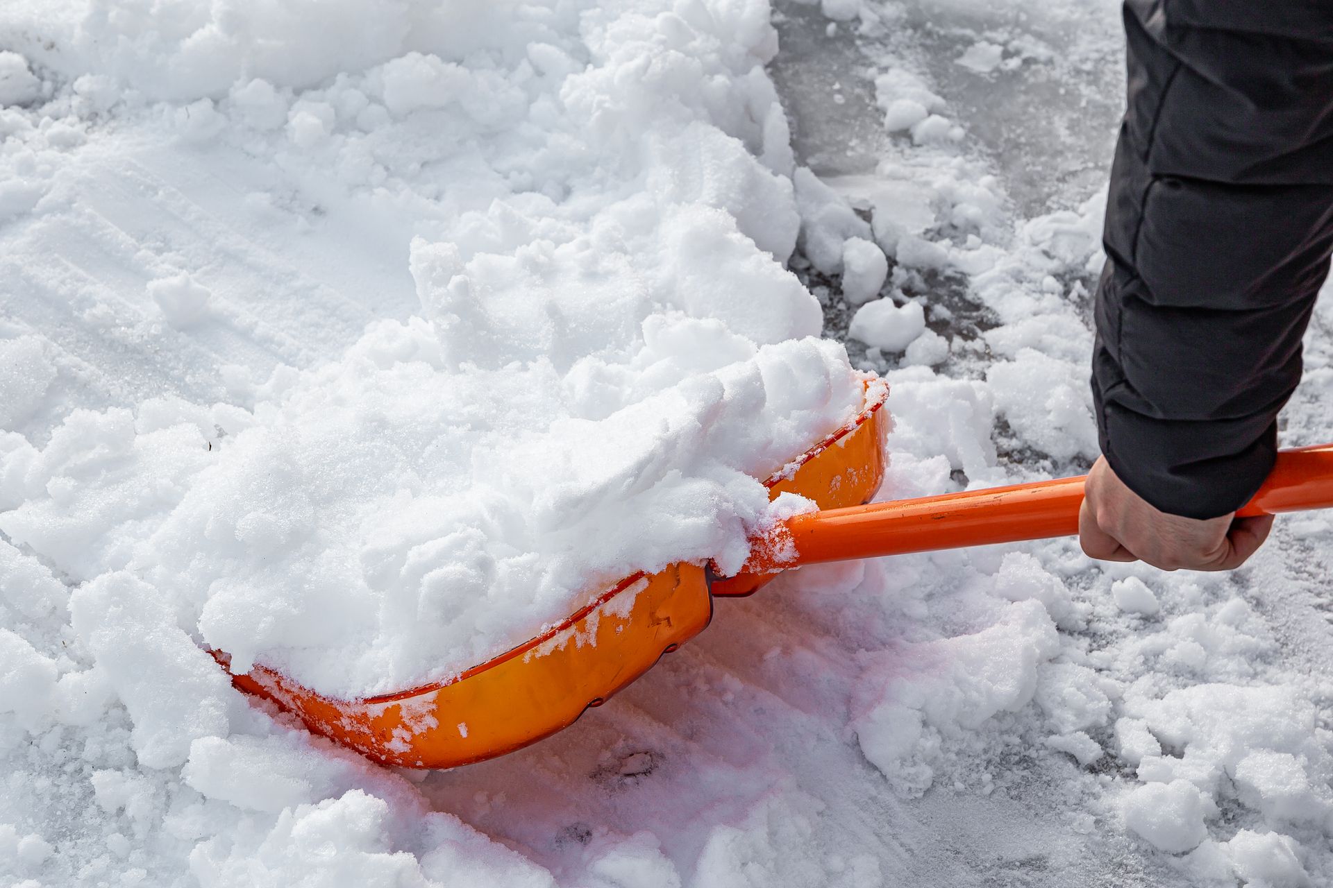 a person is shoveling snow from the ground with an orange shovel .