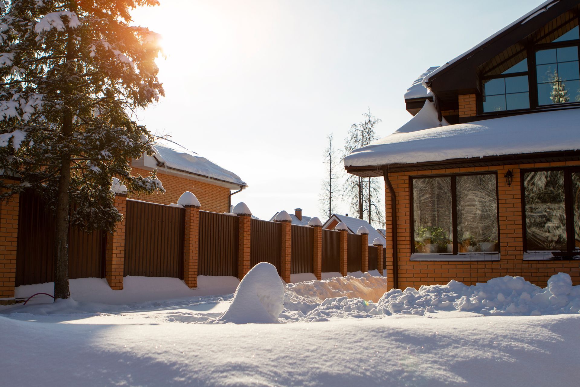 a brick house covered in snow with a wooden fence in the background .