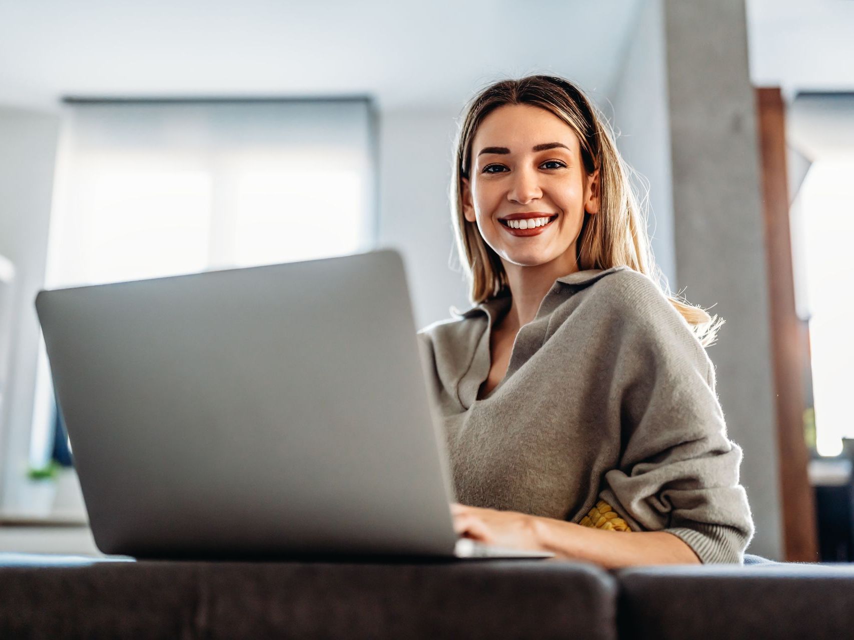 A woman is sitting on a couch using a laptop computer.