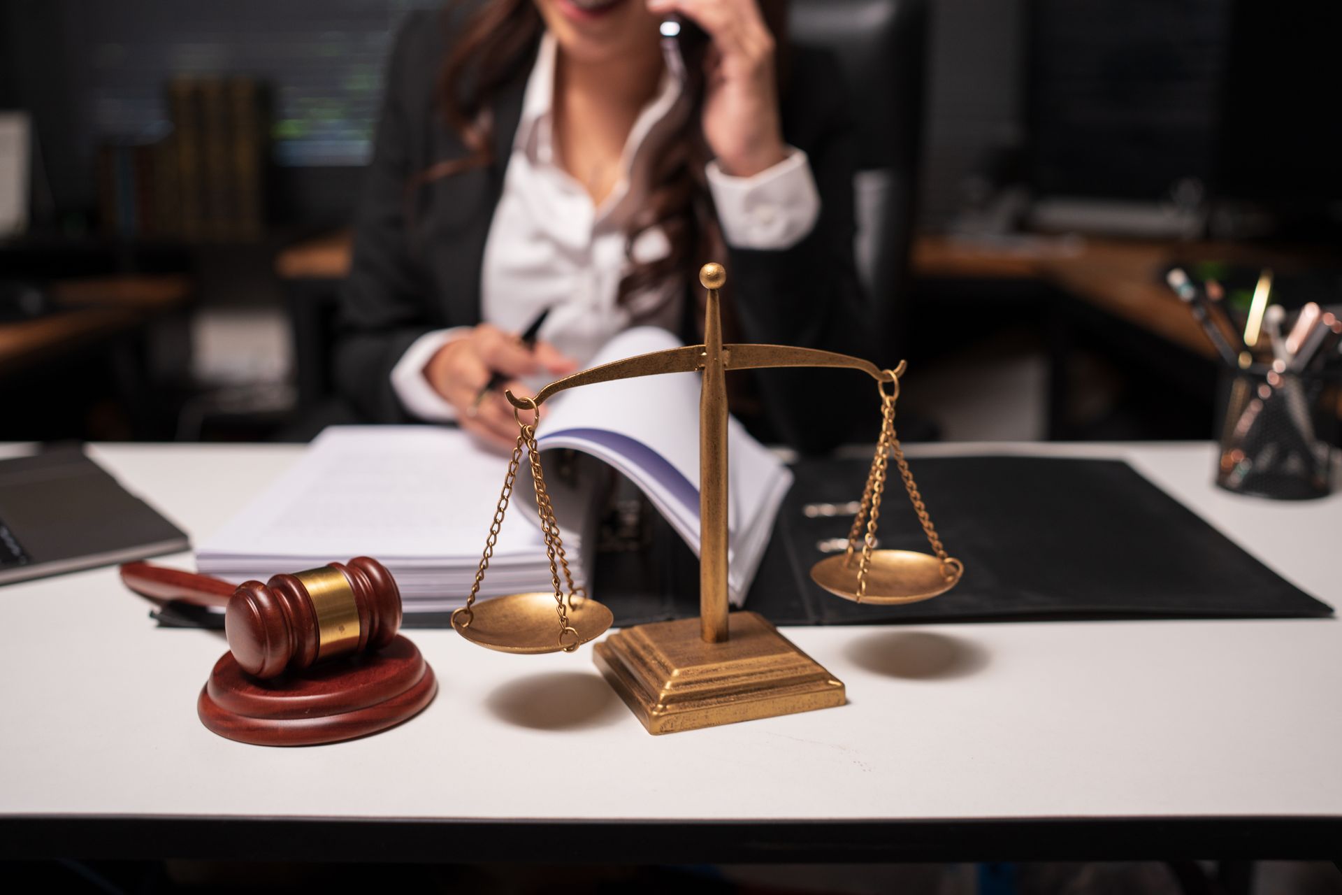 Gavel and scales on a desk with a blurred lawyer on the phone in the background.