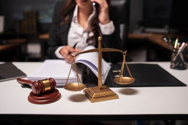 Gavel and scales on a desk with a blurred lawyer on the phone in the background.