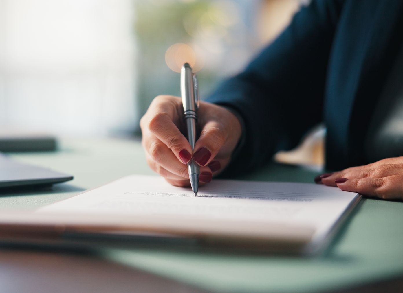 Person's hand with red nail polish writing on a white paper with a silver pen.