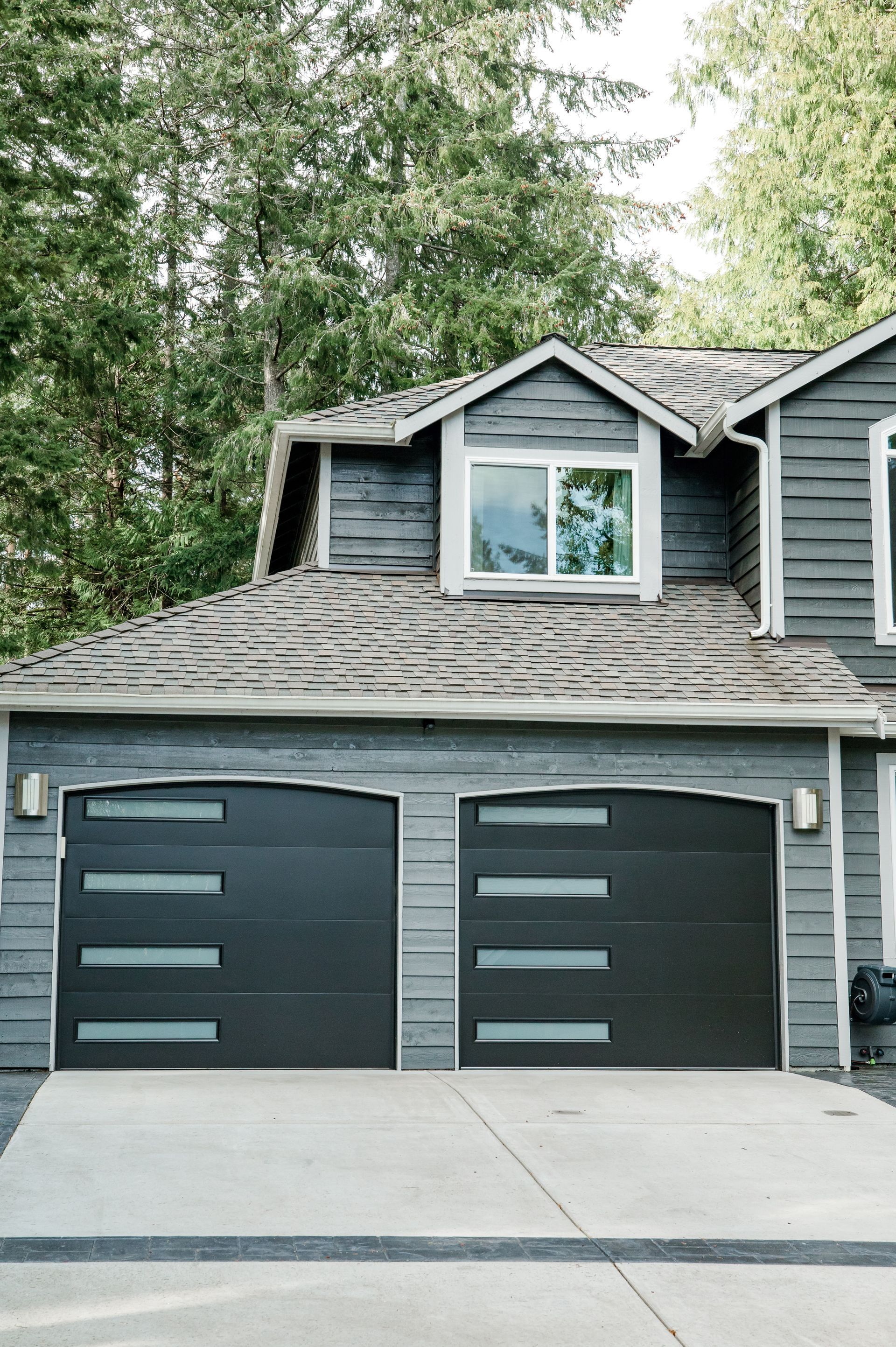 A gray house with two black garage doors and a window.