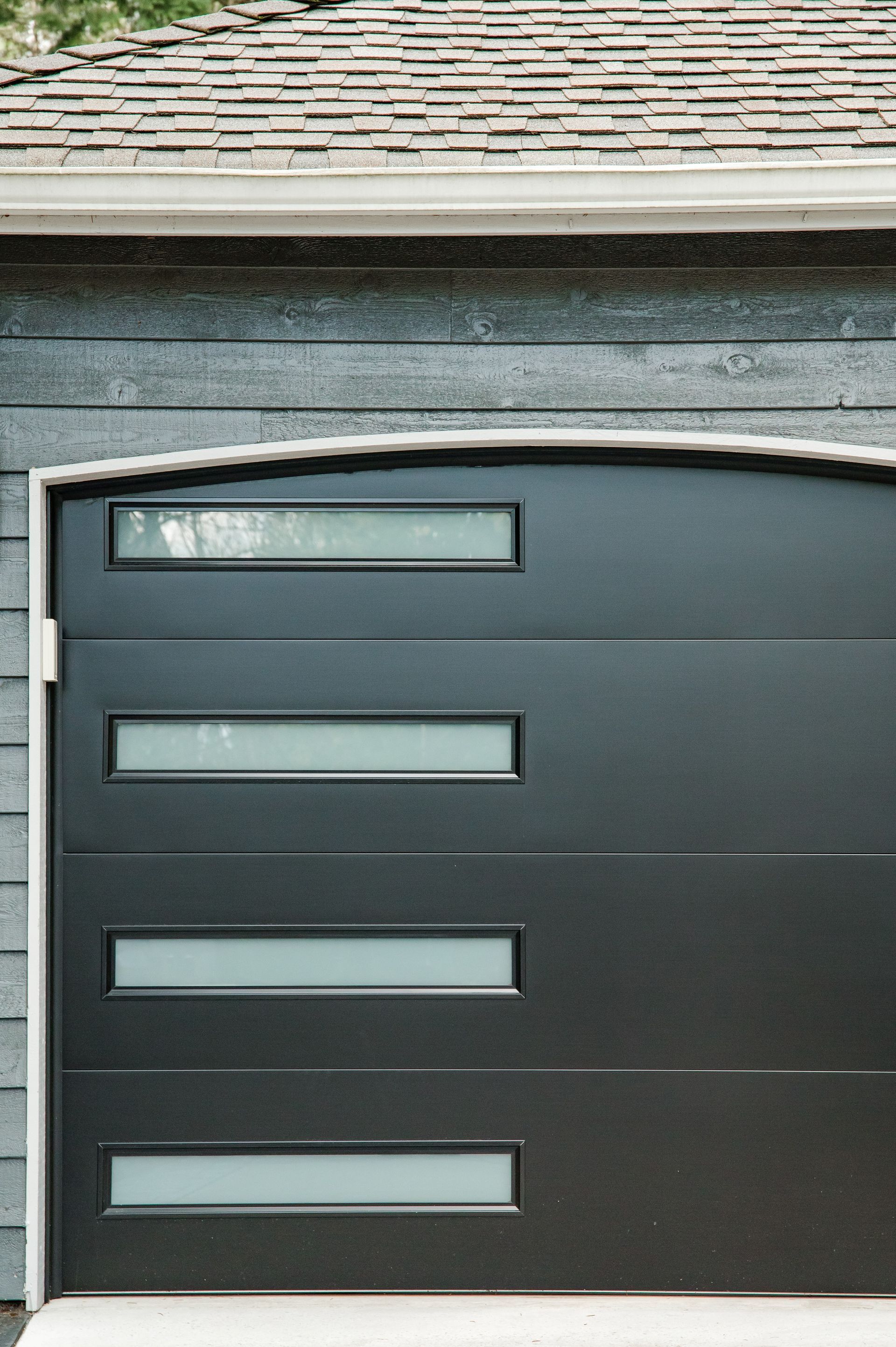 A black garage door with three windows on the side of a house.