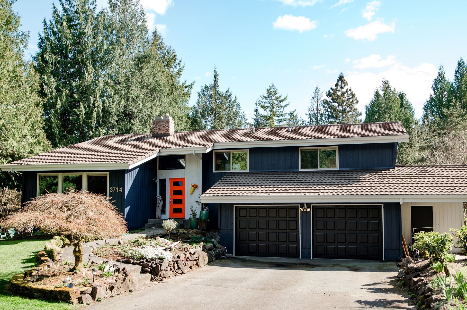 A blue house with an orange door is surrounded by trees