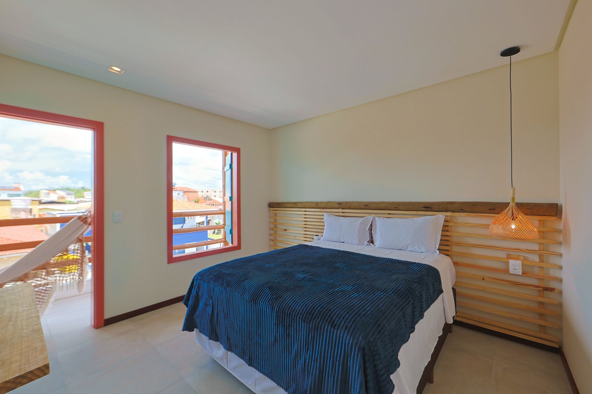 Um quarto com uma cama, duas janelas e uma varanda.