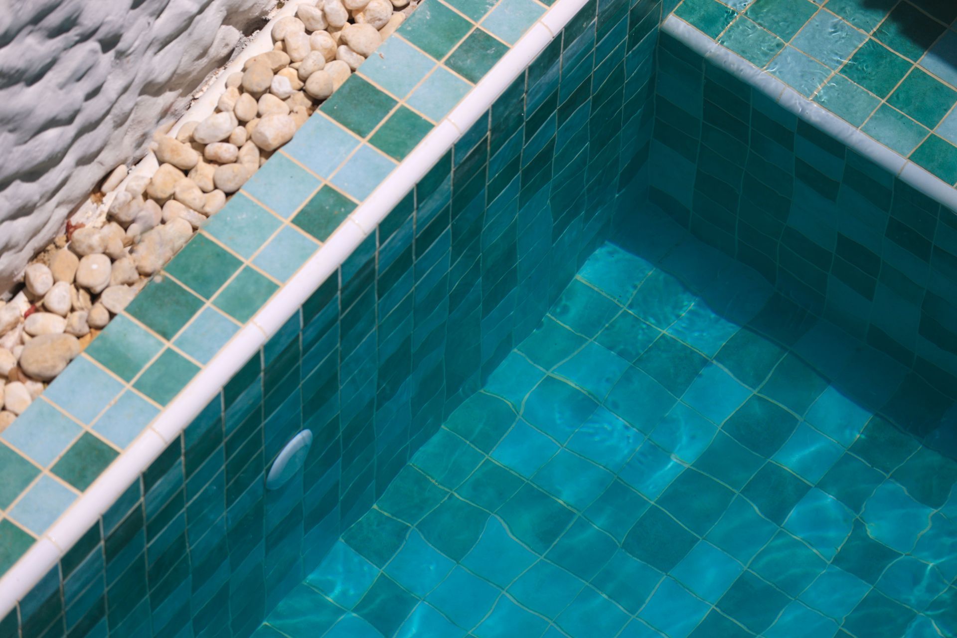 Uma piscina com azulejos azuis e pedras na borda.