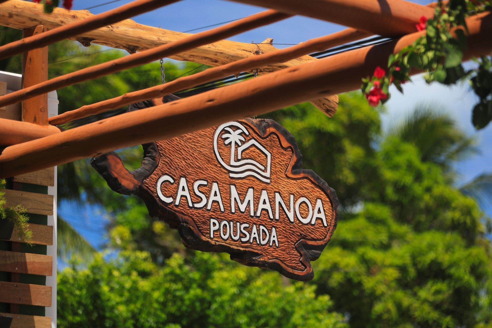 Uma placa de madeira da pousada casa manoa está pendurada em uma estrutura de madeira.