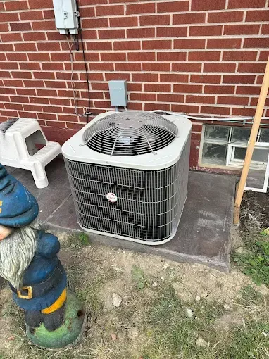 Air conditioner unit on a concrete pad next to a brick wall, garden gnome in foreground.