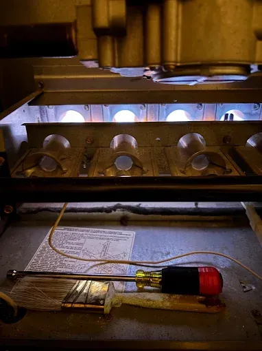Furnace interior with lit burners, a screwdriver, and a paper sheet.