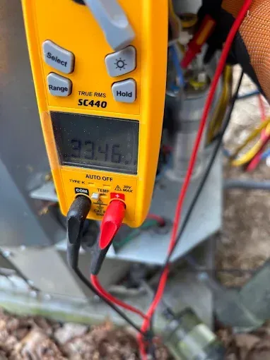 Multimeter measuring 23.46 amps on air conditioning unit wires, yellow meter, black and red leads.