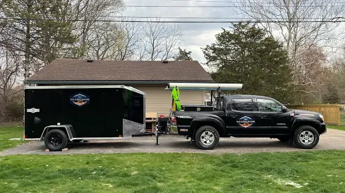 Black truck towing a black trailer in front of a house.