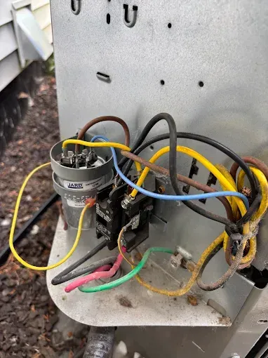Close-up of HVAC unit electrical components: capacitor, contactor, wires. Yellow, brown, blue, green wires.