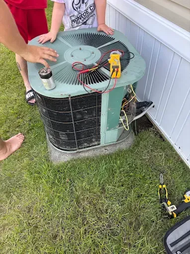 People examining an air conditioner unit on grass with tools and a multimeter.