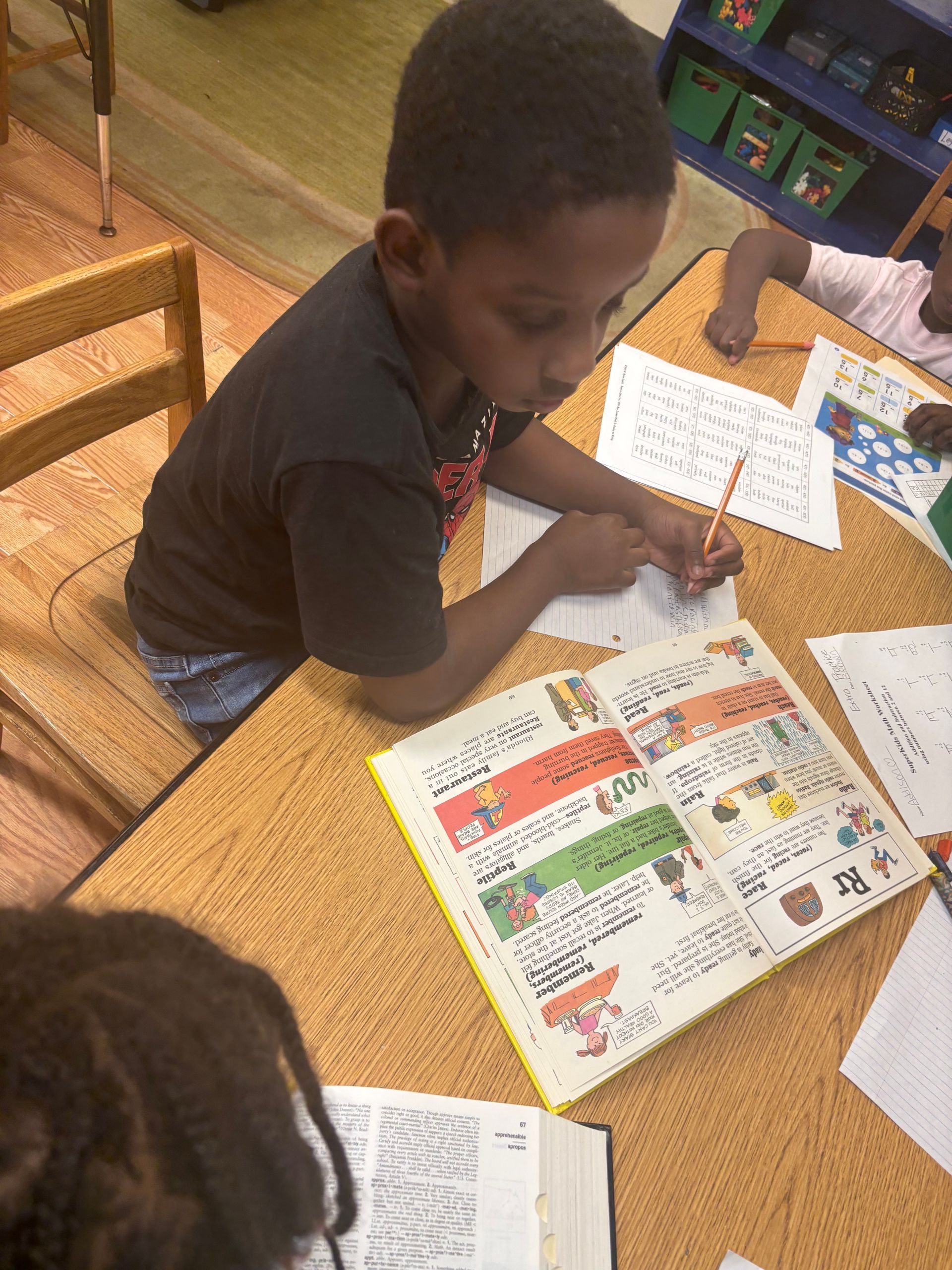 A woman is smiling while holding a clipboard in a classroom.