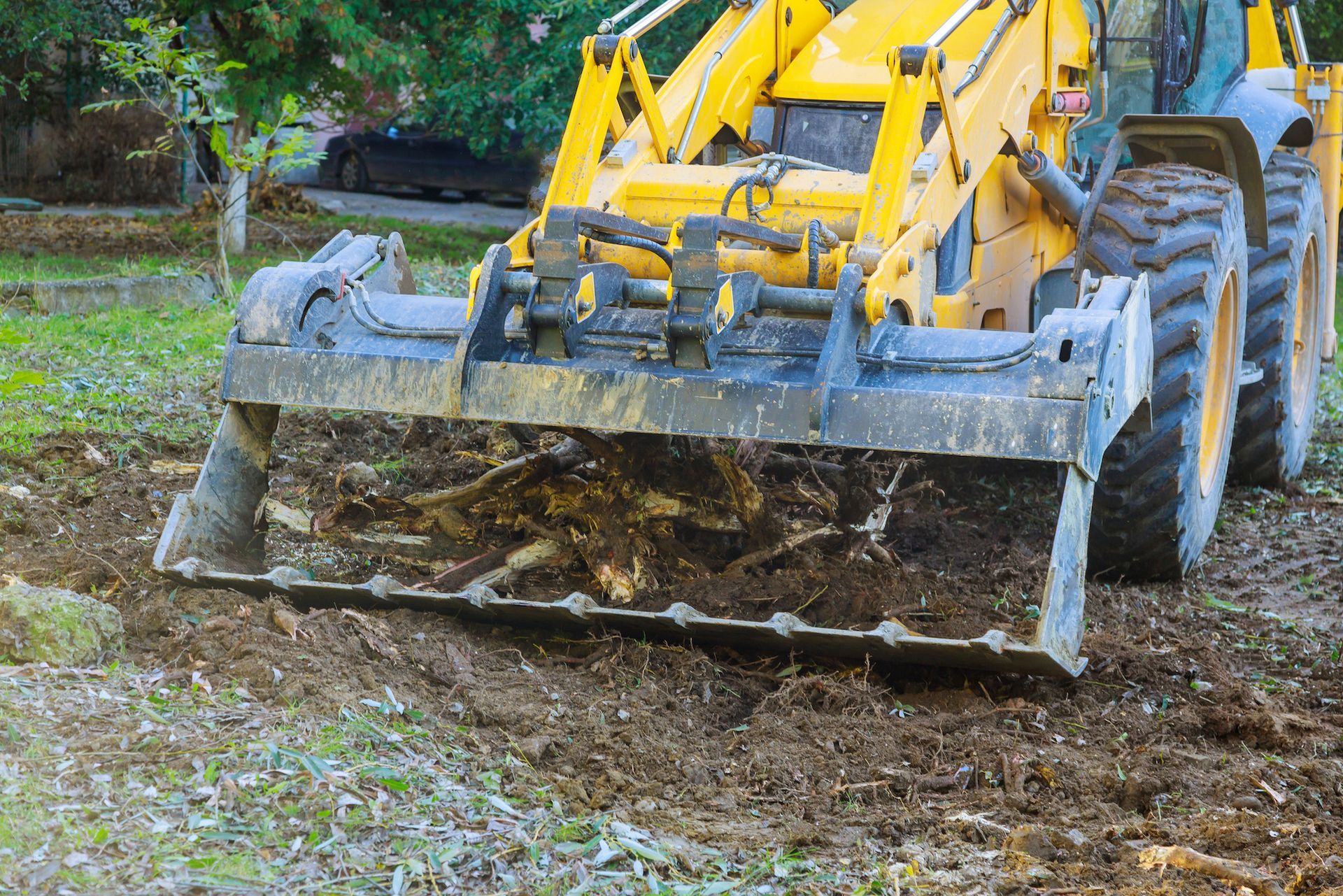 Person in reflective vest uses a leaf blower to move fallen leaves on a paved surface.